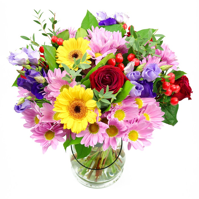 A vibrant, garden-style bouquet stands tall in a clear glass vase, set before a plain white background that enhances every colour shift and subtle texture, evoking the fresh, open feel of a stroll through King Edward VII Park in Brent. At its heart, deep red roses bloom in velvety spirals, drawing you into their rich, romantic depths and grounding the entire arrangement. Close by, yellow gerbera daisies with dark brown-orange centres become immediate focal points, their broad, round faces like little suns that beam energy and happiness outwards. Surrounding these central stars, clusters of pink and soft lavender daisy-form chrysanthemums add generous volume; their many fine petals and bright yellow centres lend a delicate, almost feathery quality that softens the bolder hues. Threaded elegantly throughout are purple and lilac lisianthus, their slender stems bearing bell-shaped blossoms with gently ruffled edges that bring a cool refinement and fluid movement. Nestled between the flowers are bright red hypericum berries, small and glossy, dotting the bouquet with playful, bead-like accents that introduce extra character and dimension. Layers of foliage in mixed greens cradle the blooms-broad, darker leaves offering depth and structure, while lighter, more delicate sprigs suggest freshness and subtle motion, as if stirred by a gentle breeze. The clear vase reveals the neatly aligned stems and clean water, hinting at the precise, experienced hand behind the natural arrangement. The bouquet's overall impression is joyful and inviting, perfect for celebrating a birthday in Wembley Park, sending congratulations to a new home in Neasden, or creating a welcoming centrepiece on a dining table anywhere in Brent, where friends and family gather.